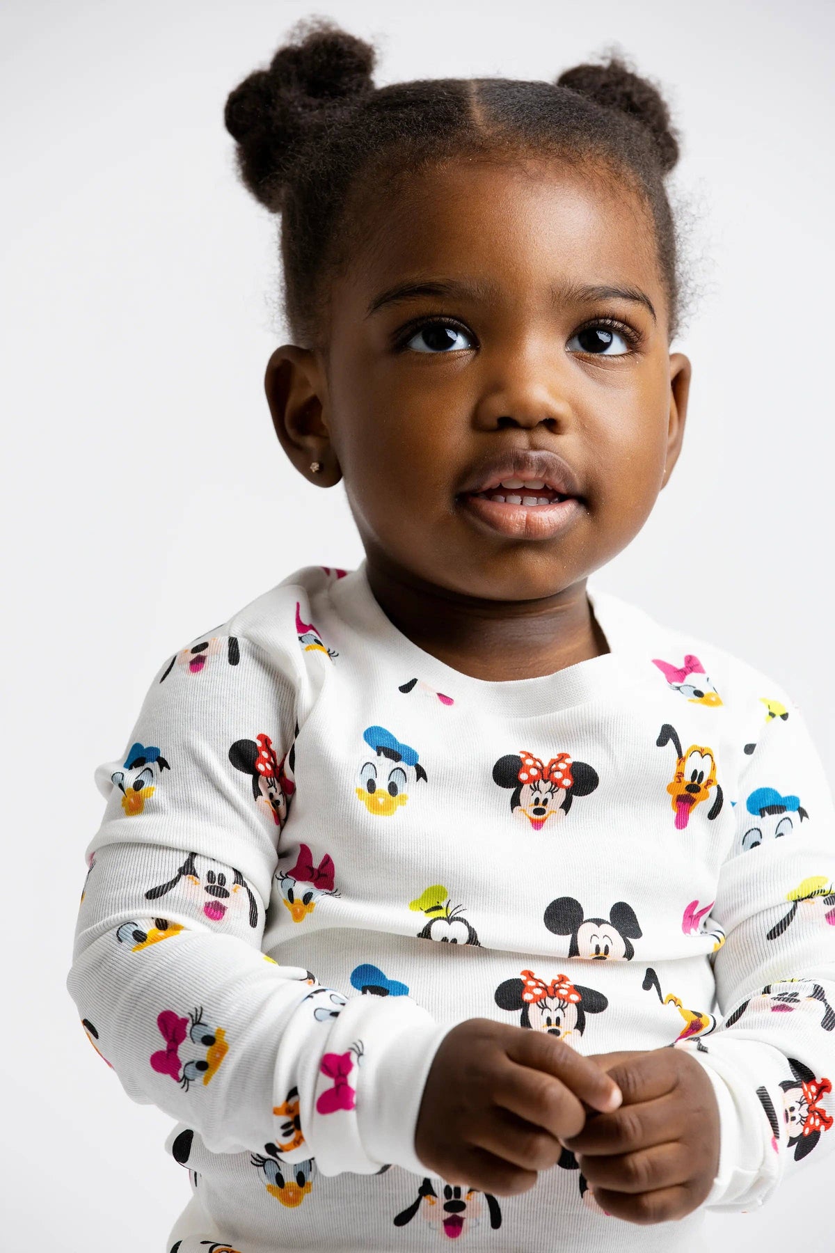 Child wearing a white long-sleeve shirt with colorful cartoon character prints on a plain background