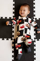 Baby wearing a black and white checkered onesie with vehicle patterns on a foam puzzle mat.