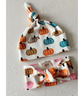 A baby hat and matching headband set by Slix Baby, featuring a white fabric print of orange, brown, and teal pumpkins. The hat has a knotted top, and the headband has a large bow.