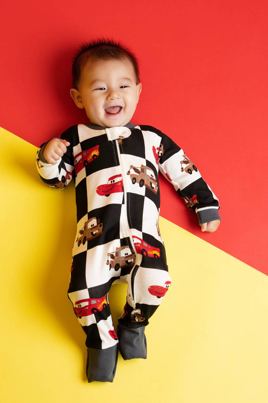 Child wearing a black and white checkered onesie with car designs on a red and yellow background