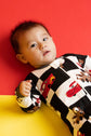 Baby wearing a black and white patterned onesie with cartoon characters against a red background