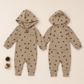 A baby hooded one-piece jumpsuit shown from both front and back views, in a warm beige color with a dark brown bear print pattern. The front view shows a snap-button closure on the chest, a chest pocket, and a zipper, while the back view shows two front pockets.