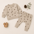 A baby two-piece outfit set consisting of a long-sleeve henley shirt and matching pants, laid flat on a light cream background. The set is beige with a brown acorn and pinecone pattern.