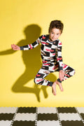 Child wearing a colorful checkered outfit jumping on a yellow background