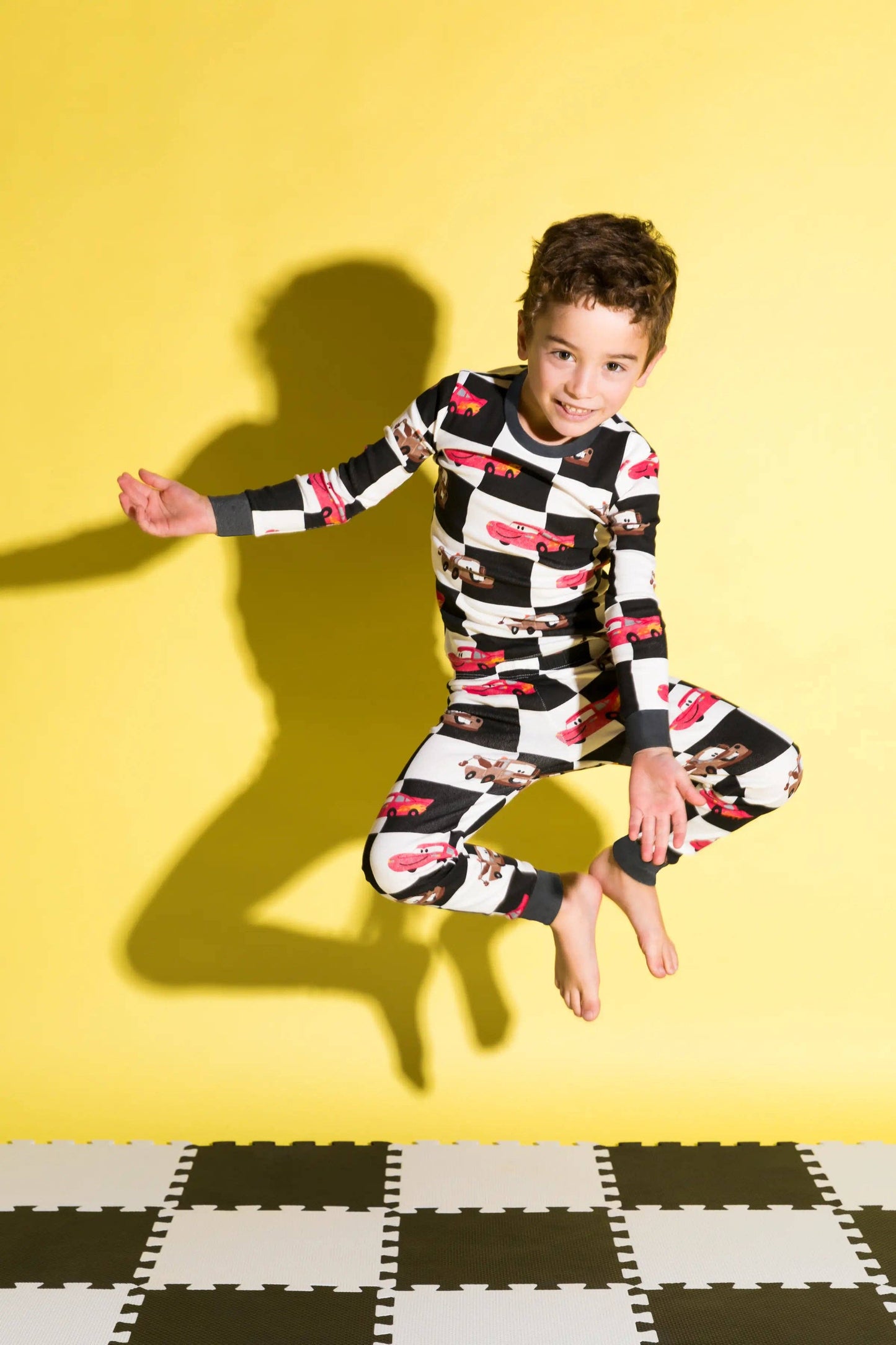 Child wearing a colorful checkered outfit jumping on a yellow background