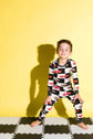Child wearing a black and white checkered onesie with red car pattern on a yellow background