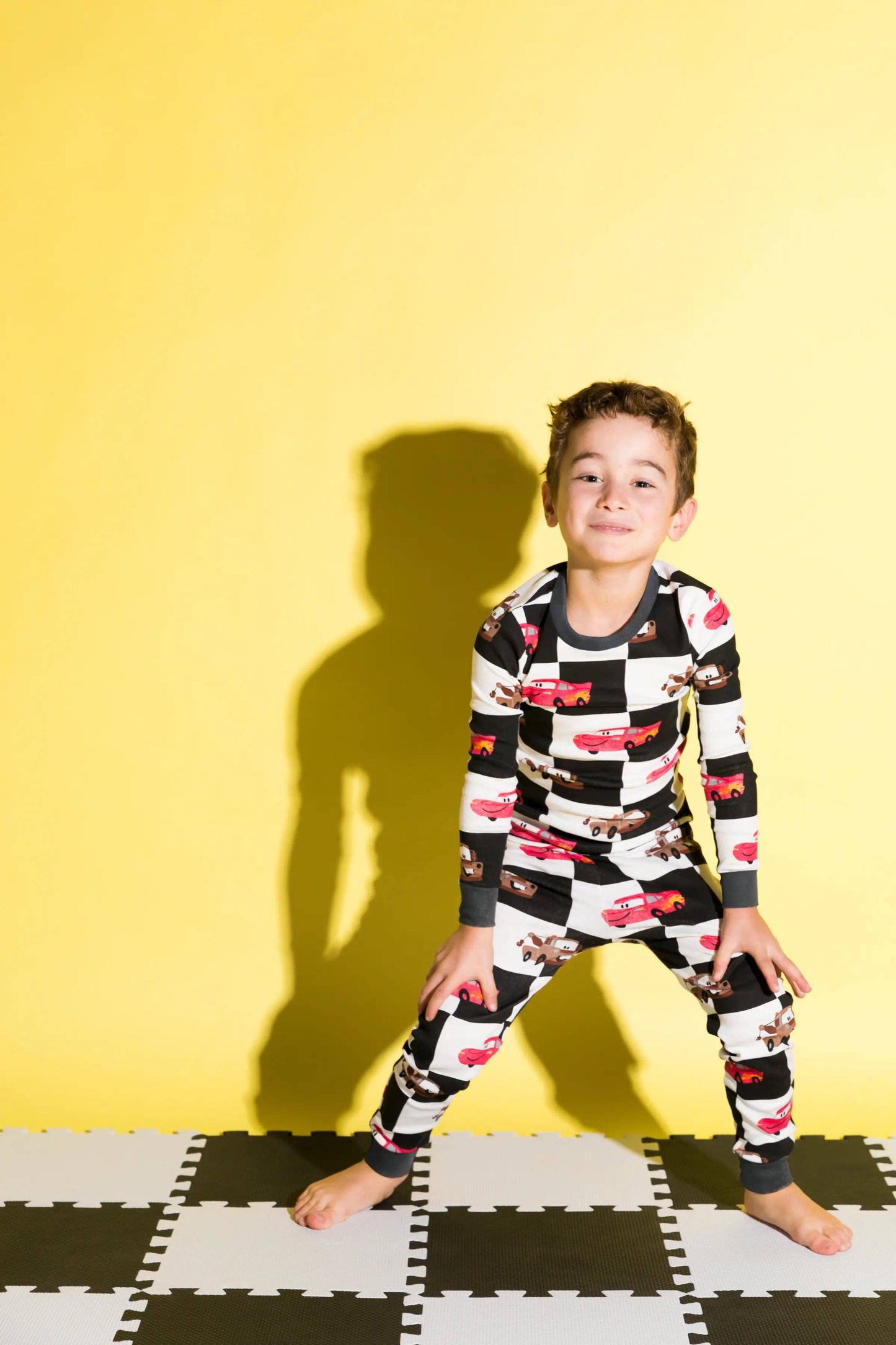 Child wearing a black and white checkered onesie with red car pattern on a yellow background