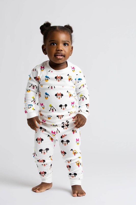 Child wearing a white pajama set with colorful character prints on a plain background